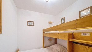 Ein kleines Zimmer mit einem Einzelbett, einem Stockbett und einem hölzernen Kopfteil. An der Wand hängen zwei gerahmte Bilder und über dem Bett befindet sich ein kleines Regal.