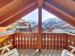Ein Balkon mit Holzgeländer und Blick auf schneebedeckte Berge und Gebäude.