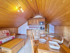 Ein gemütlicher Dachbodenraum mit Holzwänden und -decke, einer Küchenzeile, einem Esstisch für vier Personen und einem Sofa mit gemustertem Bezug.