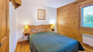 Ein Zimmer mit Holzwänden, einem Bett, zwei Nachttischlampen, einem gerahmten Bild an der Wand und einem Fenster mit Blick.