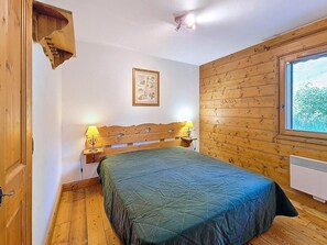 A wooden-paneled room with a bed, two bedside lamps, a framed picture on the wall, and a window with a view. - 100m from ski slopes, Ground floor, swimming pool, terrace, tv, ski locker, 32m², Les Menuires (Les Menuires)