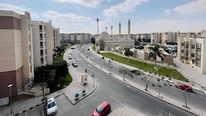Un quartier résidentiel avec des immeubles modernes, une mosquée dotée de minarets et une route bien entretenue où circulent des voitures.