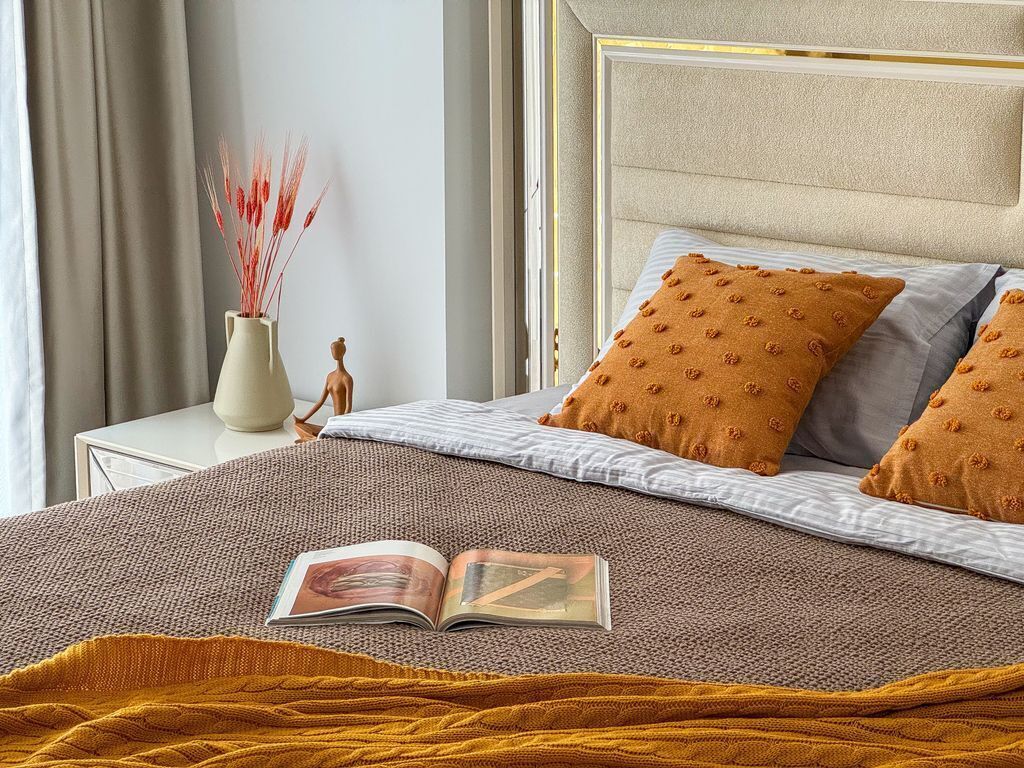 A neatly made bed with a patterned blanket, two pillows with a similar design, and a book on the bed.