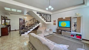 A spacious living room with a large flat-screen TV, a staircase, and a decorative mirror. - House with Pool near Attractions / Wi-Fi / Garage (Foz do Iguaçu)