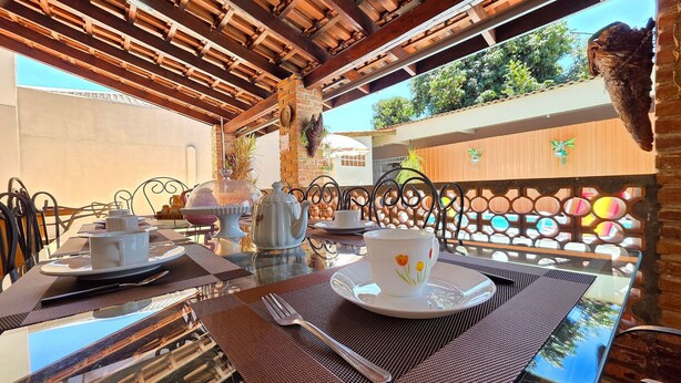 An outdoor dining area with a glass table, metal chairs, and a wooden ceiling. - House with Pool near Attractions / Wi-Fi / Garage (Foz do Iguaçu)