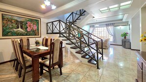 A dining area with a wooden table and chairs, a staircase with a geometric design, and a painting on the wall. - House with Pool near Attractions / Wi-Fi / Garage (Foz do Iguaçu)