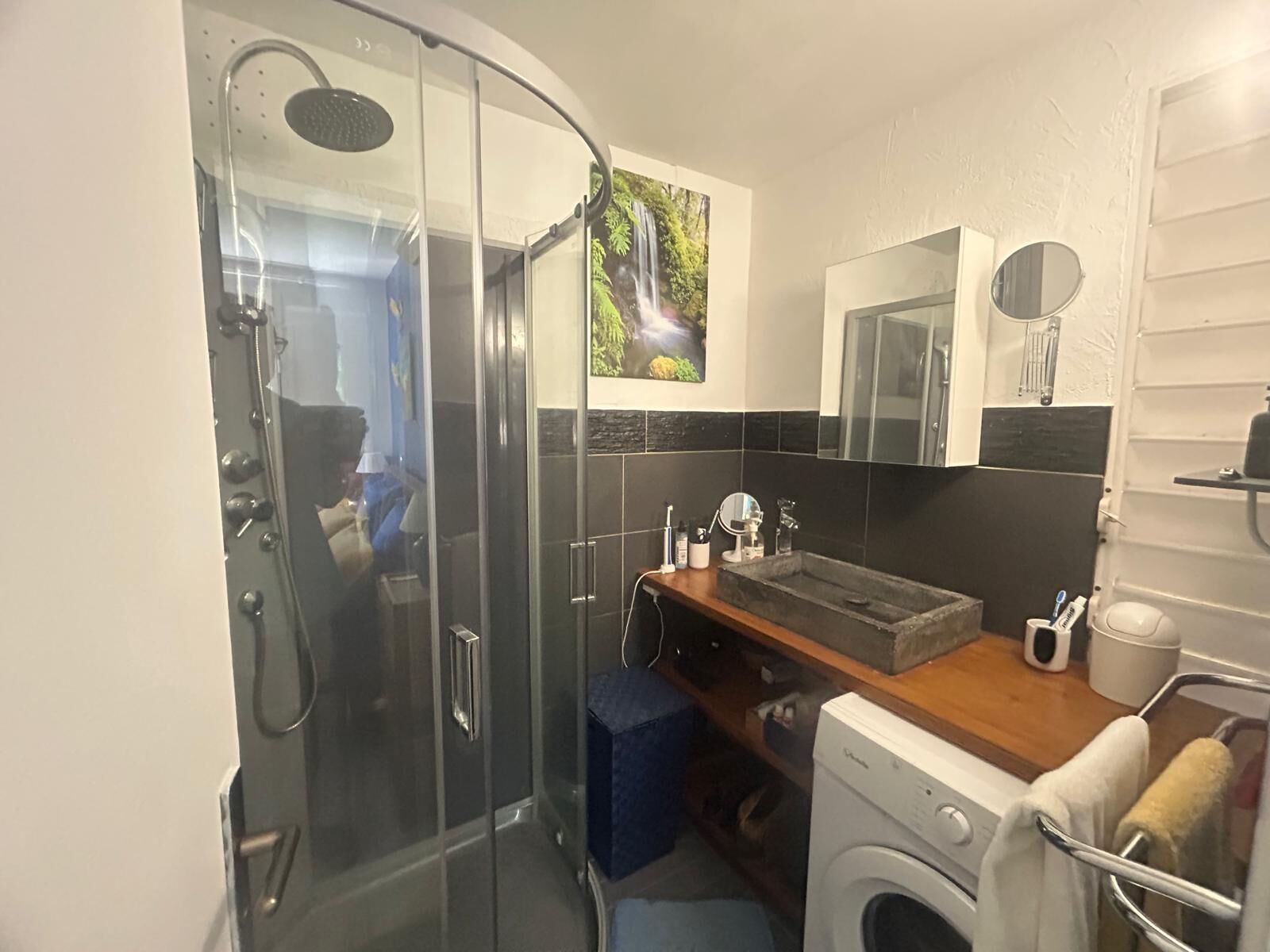 Un baño moderno con ducha acristalada, lavabo integrado, espejo y lavadora.