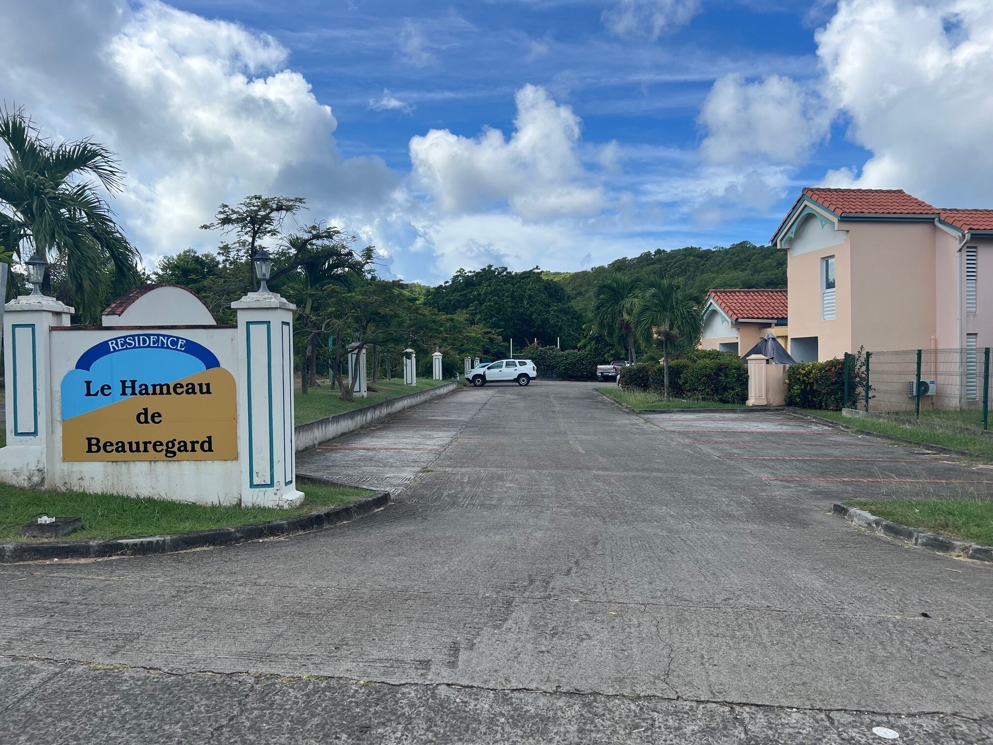 A sign for Le Hameau de Beauregard residence, a paved road, and a building with a red-tiled roof.