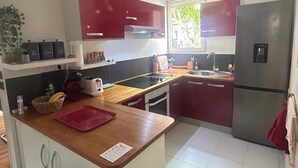 A compact kitchen with a wooden countertop, a built-in stove, a sink, and a refrigerator. - Cocon Tropical (Sainte-Anne)