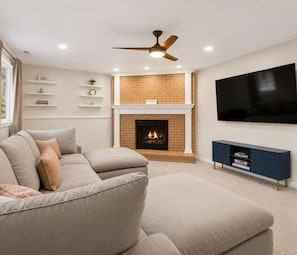 A living room with a sectional sofa, a fireplace, a mounted TV, and a ceiling fan. - 5BR + Game Room Bridge Park + Zoo Sleeps 12 (Columbus)
