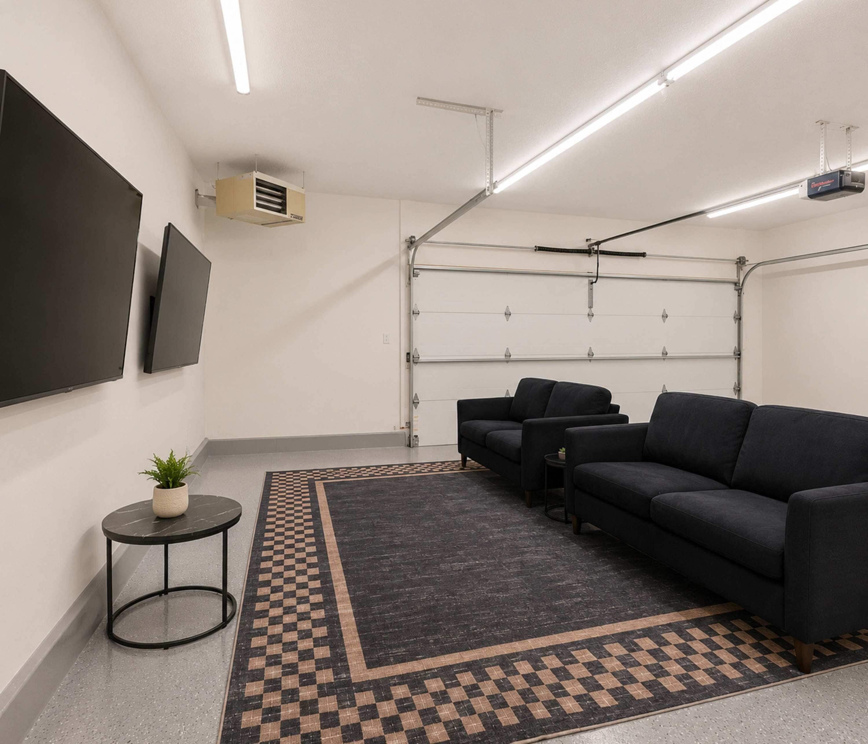 A modern home theater room with a flat-screen TV, a ceiling-mounted projector, a large garage door, and a seating area with a patterned rug.