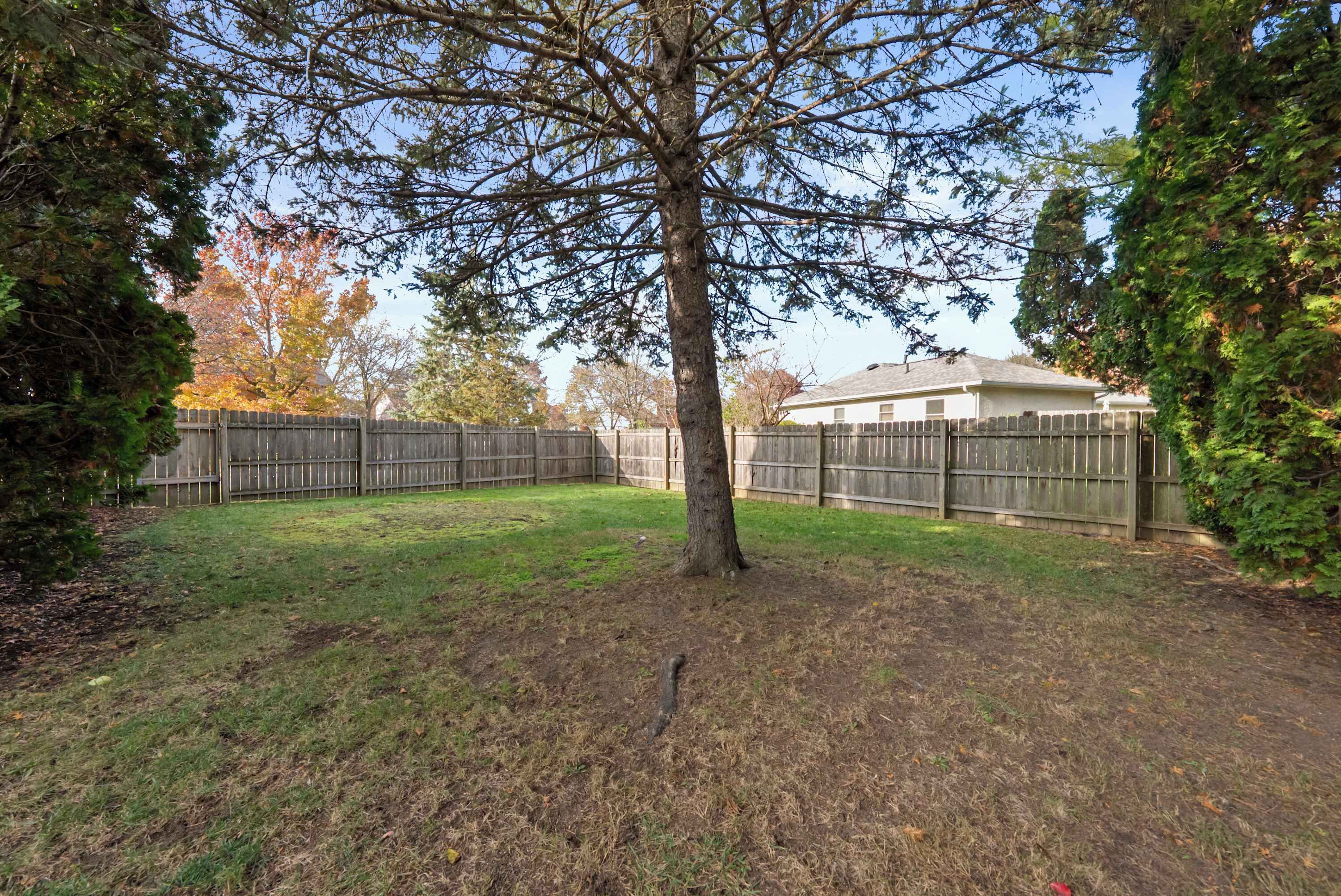 A fenced backyard with a tree, grass, and a wooden fence.