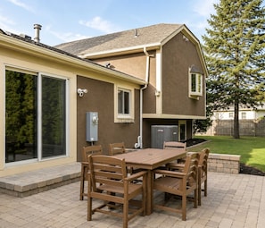 A patio with a wooden table and chairs, a covered outdoor area, and a house with a large window and a chimney. - 5BR + Game Room Bridge Park + Zoo Sleeps 12 (Columbus)