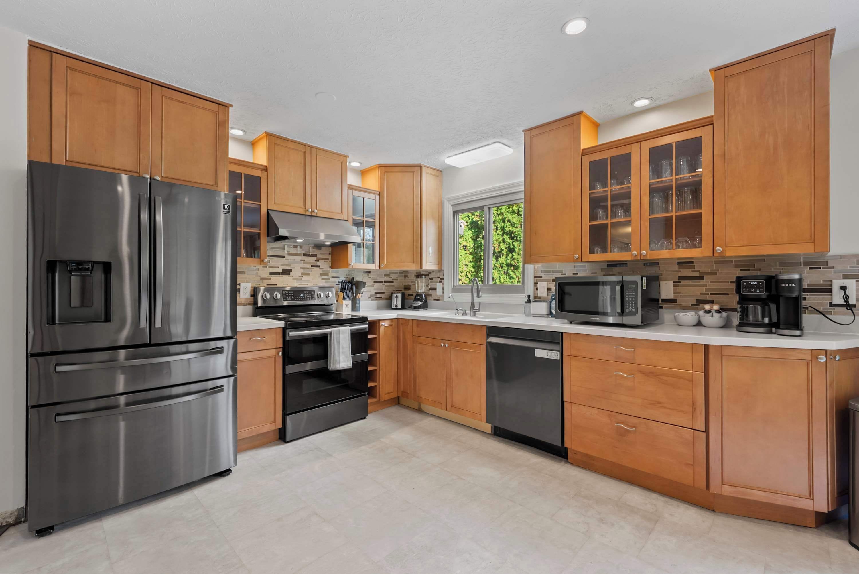 A modern kitchen with stainless steel appliances, wooden cabinets, and a large window providing natural light.