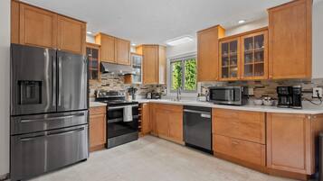 A modern kitchen with stainless steel appliances, wooden cabinets, and a large window providing natural light.