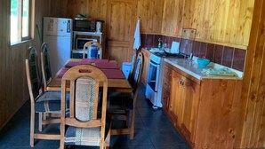 A compact kitchen with wooden cabinets, a dining table with chairs, a refrigerator, a microwave, and a stove. - Beautiful Family Cabin in Pucón (Pucon)