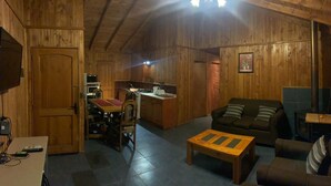 A wooden interior with a sofa, a small table, a kitchenette, and a television. - Beautiful Family Cabin in Pucón (Pucon)