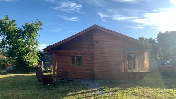 A wooden cabin with a sloped roof, a small porch with two chairs, and a clear sky. - Beautiful Family Cabin in Pucón (Pucon)