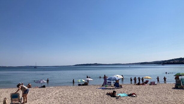 A beach with people sunbathing and swimming, umbrellas, and a clear view of the sea and distant hills. - Penthouse Cortegada (Boiro)
