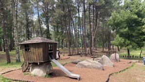 A playground with a wooden slide and play structures, surrounded by a wooded area. - Penthouse Cortegada (Boiro)