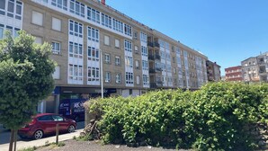 A multi-story building with large windows and balconies, a red car parked in front, and a hedge in the foreground. - Penthouse Cortegada (Boiro)