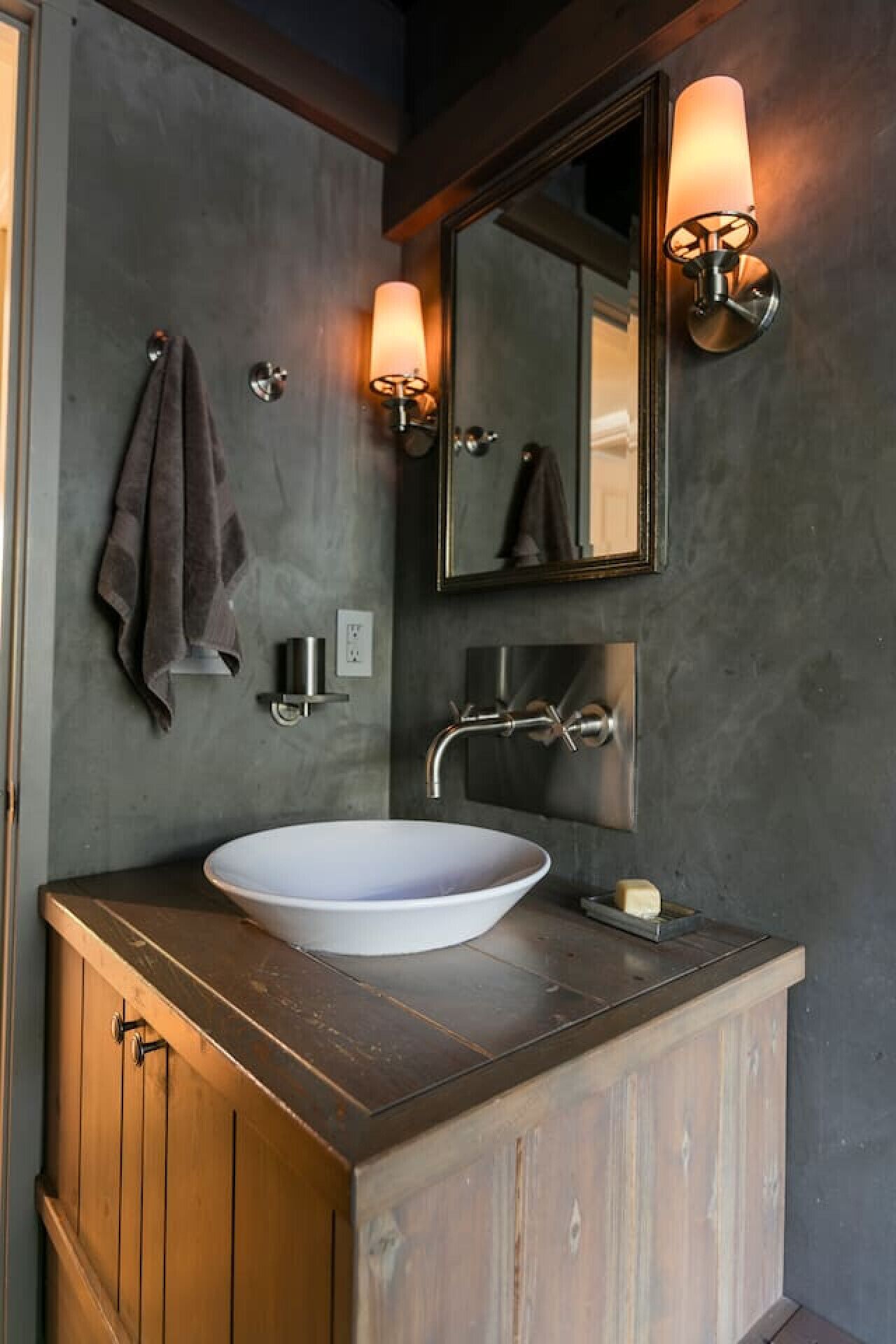 Ein modernes Badezimmer mit einem großzügigen Aufsatzwaschbecken, einem Holzwaschtisch, einem Spiegel mit Wandleuchten und einem Handtuch an der Wand.