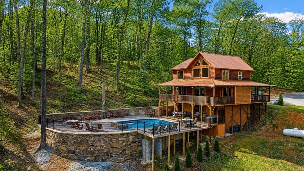 A wooden cabin with a pool, surrounded by trees. - Heated Pool (seasonal), Hot Tub, Game Room, & Mountain Views – Sleeps 12 (Sevierville)