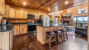 A wooden cabin interior with a kitchen, bar area, and a fireplace. - Heated Pool (seasonal), Hot Tub, Game Room, & Mountain Views – Sleeps 12 (Sevierville)