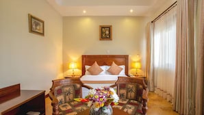 A hotel room with a bed, two chairs, a table with a vase of flowers, and two lamps. - 6Cape Guest House Kawanda  (Kampala)
