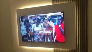 A television mounted on a wall with a group of people in the background. - 6Cape Guest House Kawanda  (Kampala)