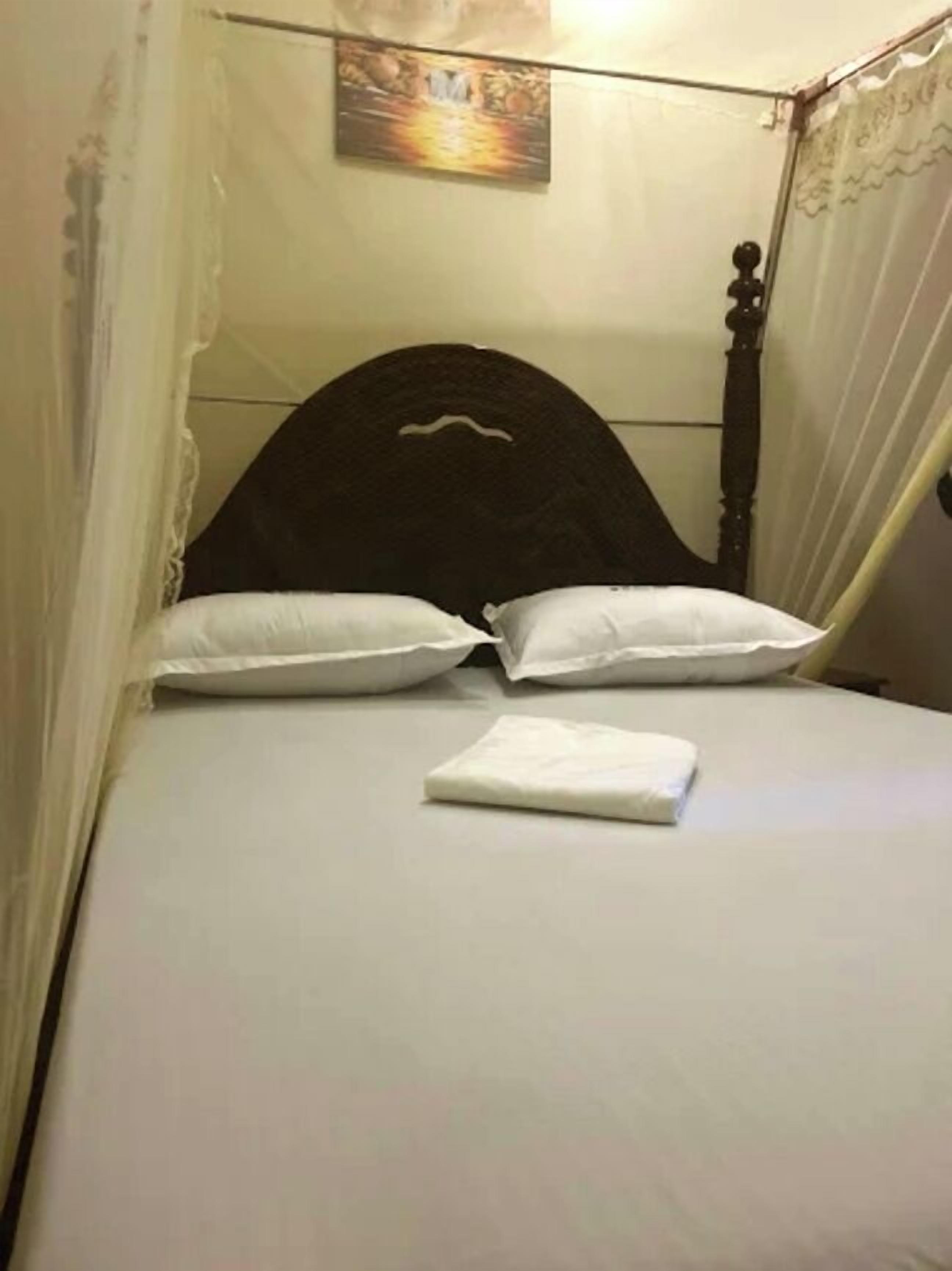Una cama con cabecera oscura, almohadas blancas y una manta blanca doblada con cuidado.