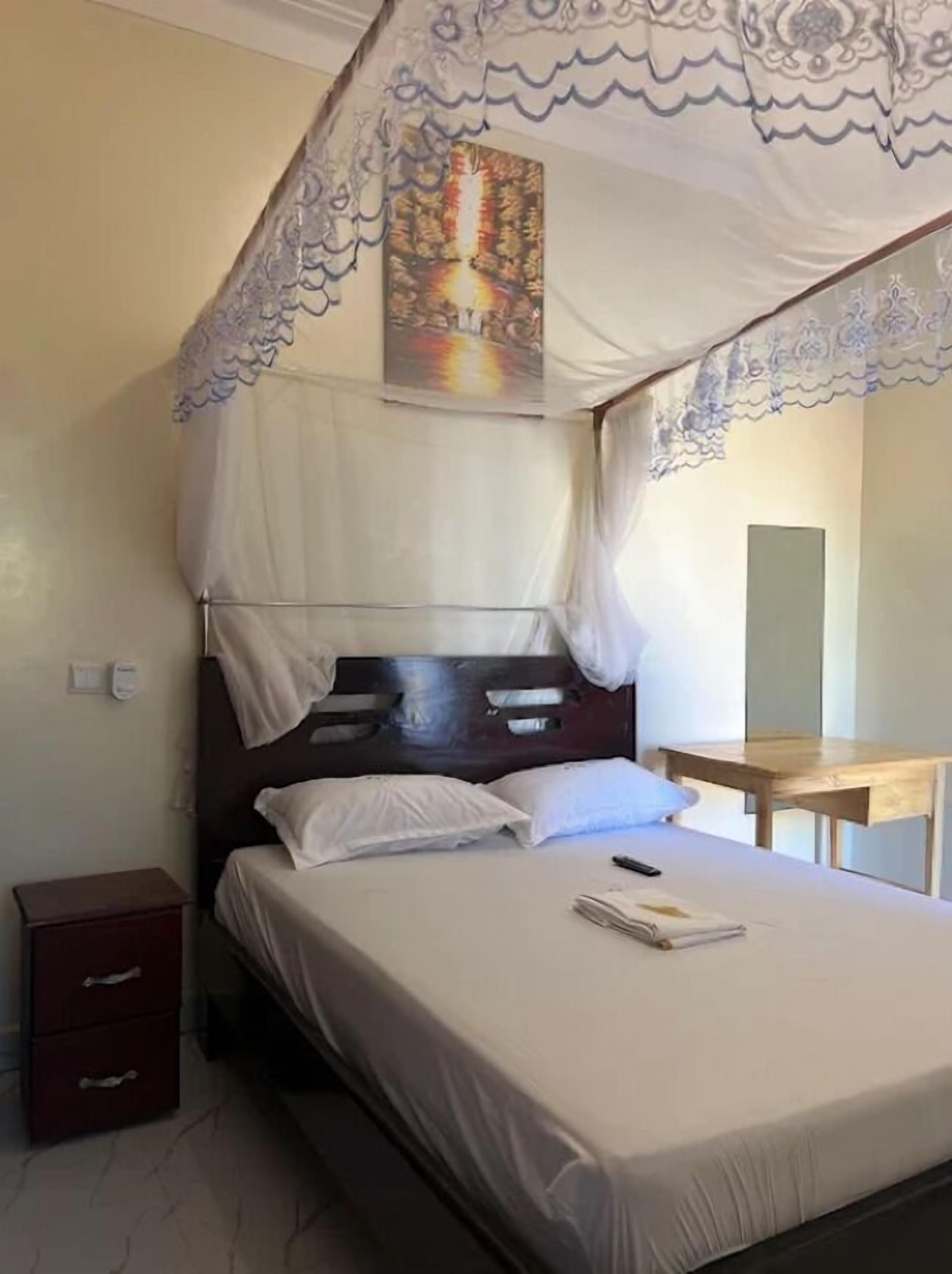 A neatly made bed with a canopy, a bedside table, and a small wooden nightstand.