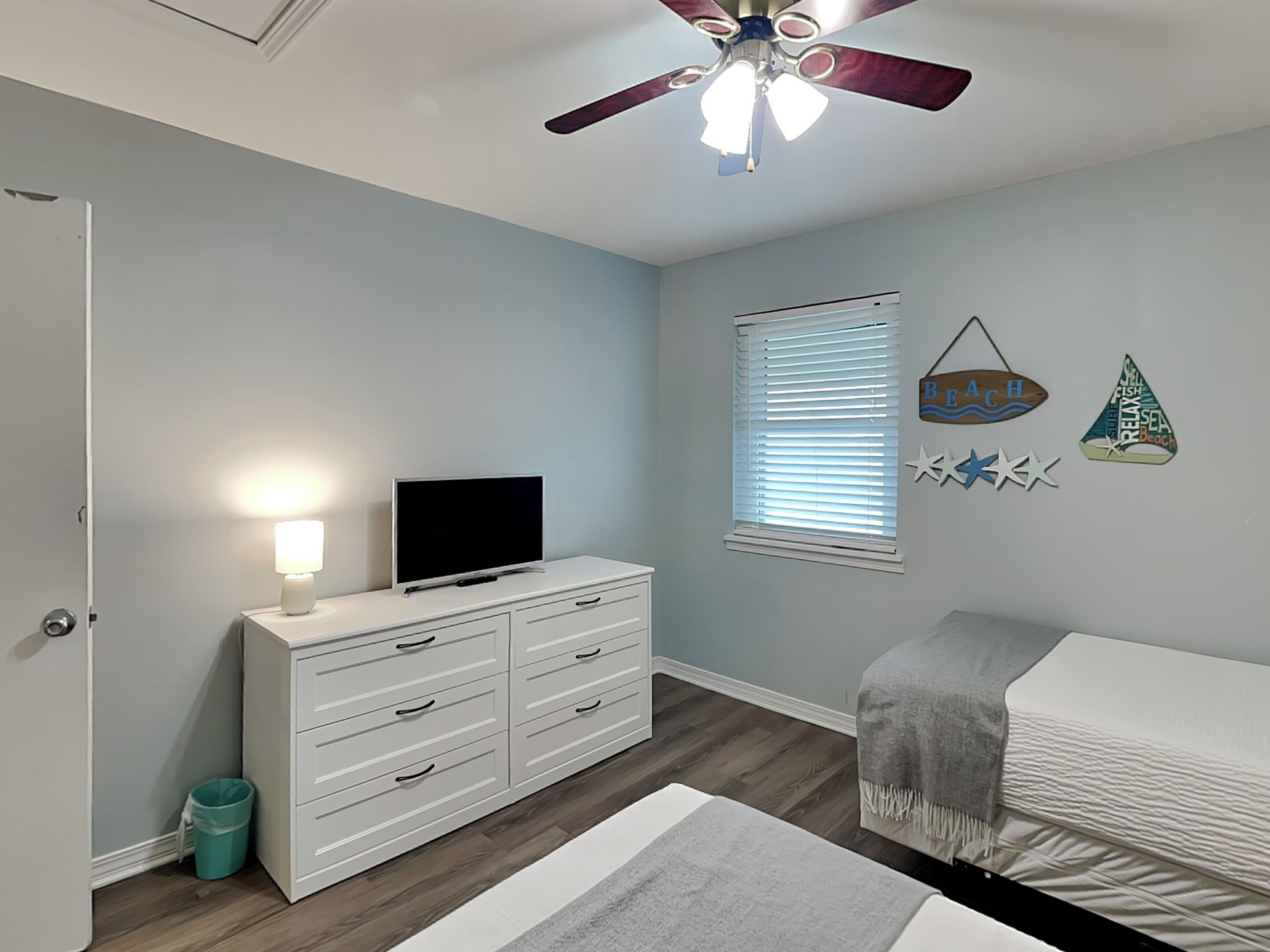A bedroom with a bed, a dresser, a TV, a ceiling fan, and a window with blinds.