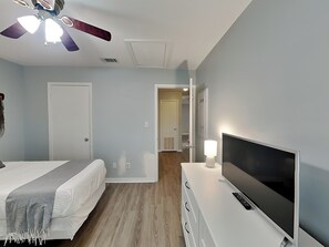 A bedroom with a bed, a TV on a dresser, a ceiling fan, and a door leading to another room. - Ocean Echo #303 (Gulf Shores)