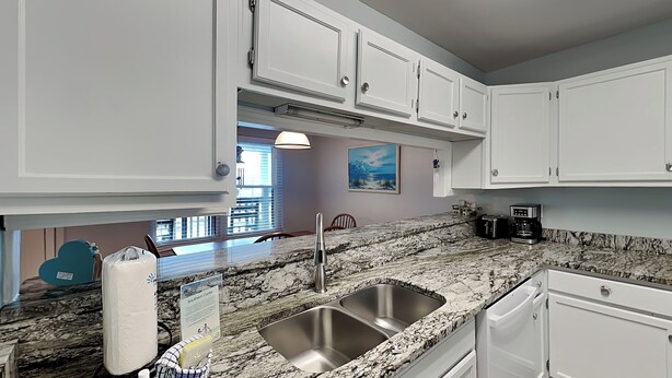 A kitchen with white cabinets, a granite countertop, a stainless steel sink, and a coffee maker. - Ocean Echo #303 (Gulf Shores)