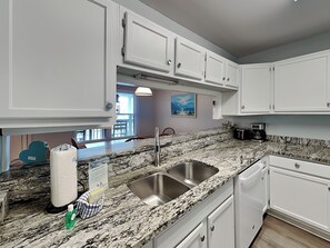 A kitchen with white cabinets, a granite countertop, a stainless steel sink, and a coffee maker. - Ocean Echo #303 (Gulf Shores)