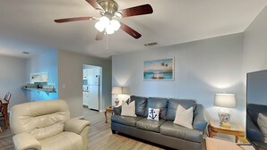 A living room with a beige leather chair, a grey sofa with nautical-themed pillows, a wooden coffee table, and a ceiling fan. - Ocean Echo #303 (Gulf Shores)