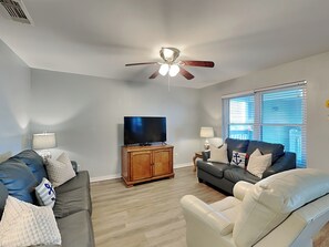 A living room with a ceiling fan, a flat-screen TV, a wooden cabinet, and two sofas. - Ocean Echo #303 (Gulf Shores)