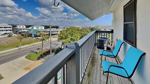 A balcony with a view of a street and buildings, featuring a row of blue chairs and a trash can. - Ocean Echo #303 (Gulf Shores)