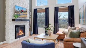 Amplia sala de estar con chimenea, ventilador de techo y grandes ventanales que ofrecen vistas al exterior.