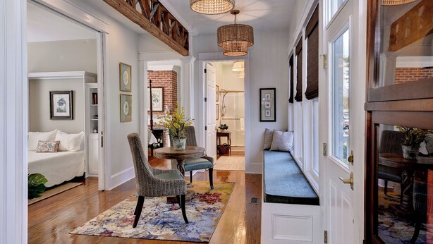 A hallway with a wooden floor, a bench, a dining area with a table and chairs, and a staircase.