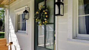 A house with a porch, a door with a wreath, and two windows with hanging lanterns.