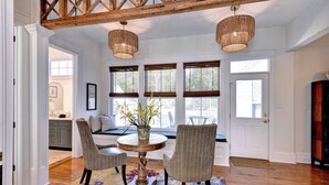 A dining area with a round table, two chairs, a vase with flowers, and a wooden ceiling beam.