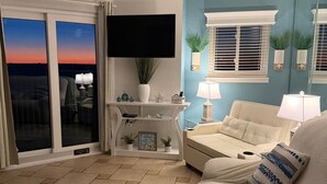 A living room with a sofa, a coffee table, a TV, and a ceiling fan. - The Coastal Turtle - Modern Beach Front Retreat (Gulf Shores)