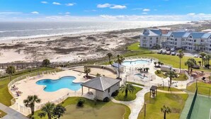 A resort with a large pool, a beach view, and multiple buildings. - The Coastal Turtle - Modern Beach Front Retreat (Gulf Shores)