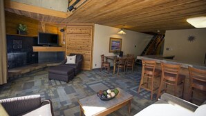 Ein gemütlicher Wohnbereich mit Kamin, Fernseher und einem Essbereich mit Holzsesseln und Tisch.