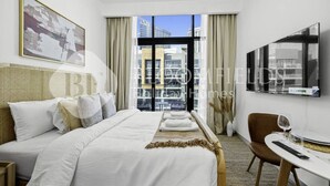 Ett hotellrum med en stor säng, en tv som är monterad på väggen, ett matbord med en stol och utsikt över staden genom fönstret.