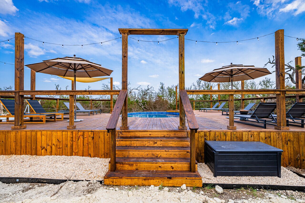 Een houten terras met een zwembad, ligbedden en parasols.