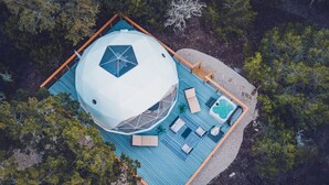 Vista aérea de una estructura en forma de cúpula con piscina, terraza y zona de estar rodeada de árboles.