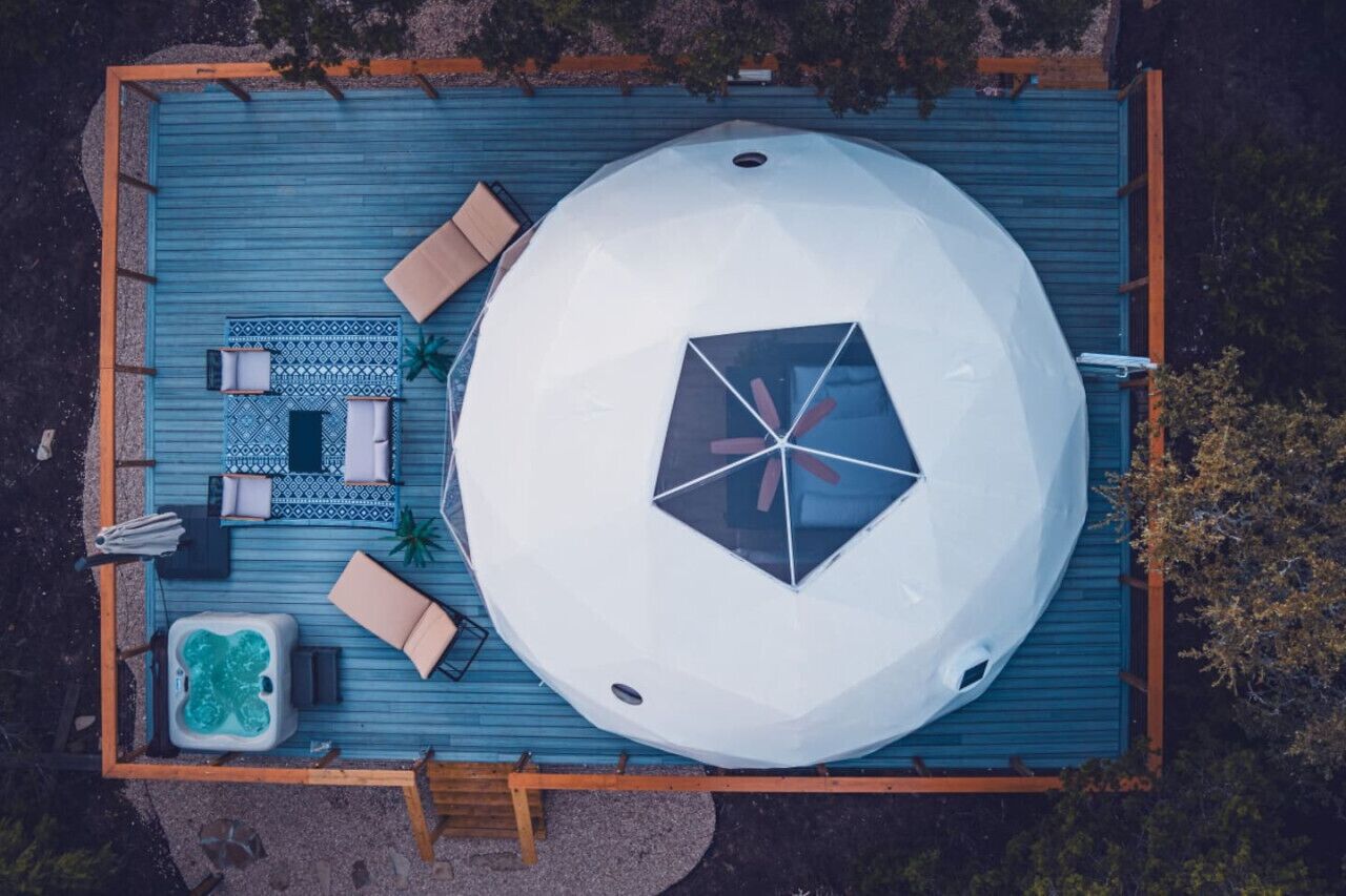Luchtbeeld van een dakzwembad met een grote witte koepelstructuur, ligbedden, een jacuzzi en een betegeld zonnedek.